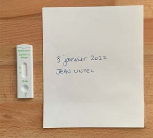 Exemple d'une photo qui comprend une cartouche de test rapide affichant un résultat positif accompagné d'un papier sur lequel le nom et la date du jour sont inscrits à la main.